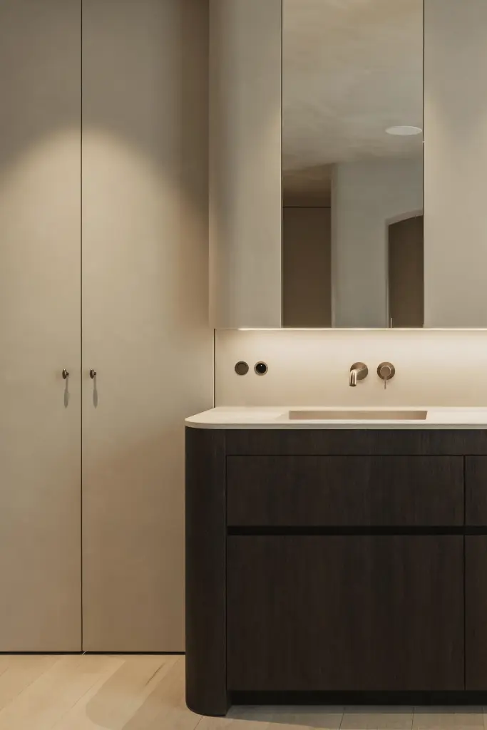 Badkamer met wastafelmeubel in donker eiken, wandkranen en een spiegelkast onder de dakhelling, Hoeve in Hansbeke, interieur Laura Calleeuw