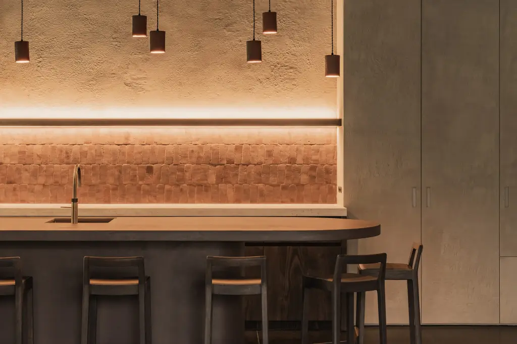 Terracotta hanglampen en tegelwand met ledlijn boven het kookeiland met kraan, Hoeve in Hansbeke, interieur Laura Calleeuw