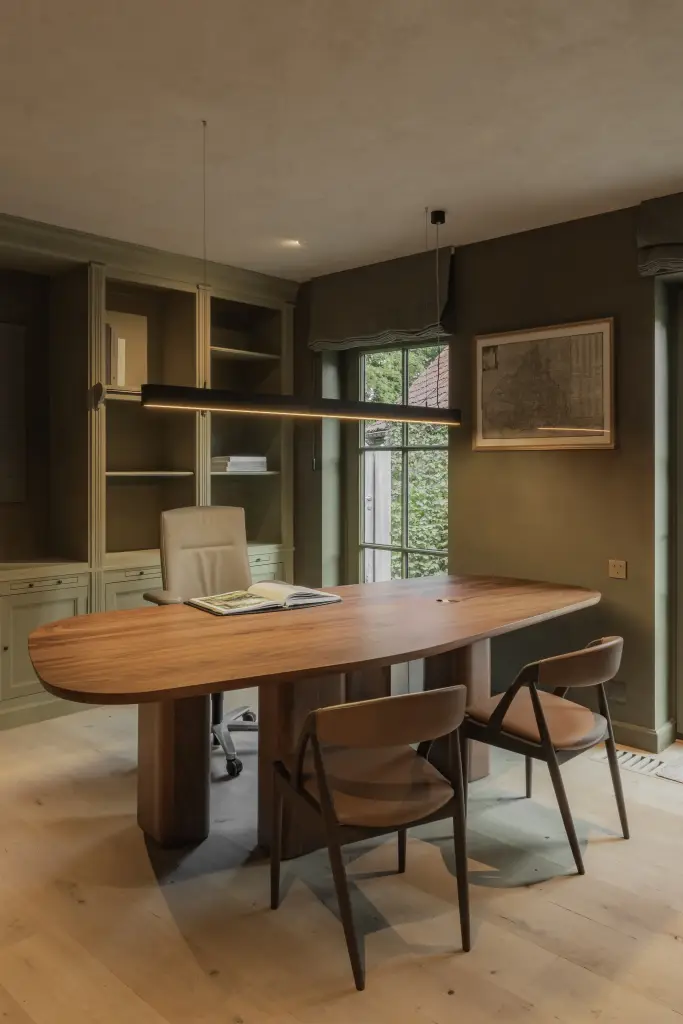 Werkkamer met ovale notelaren tafel, stoelen, boekenkasten en groen geschilderde wanden, Hoeve in Hansbeke, interieur Laura Calleeuw