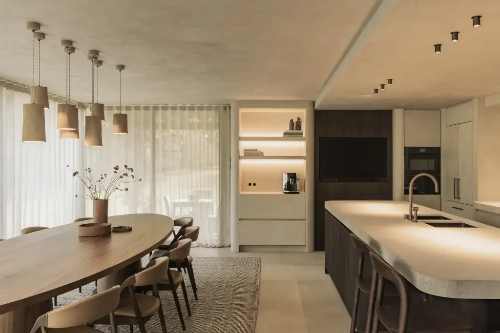 Eetkamer met lange ovale notelaren tafel, hanglampen in aardewerk en keukeneiland met natuurstenen blad, Hoeve in Hansbeke, interieur Laura Calleeuw