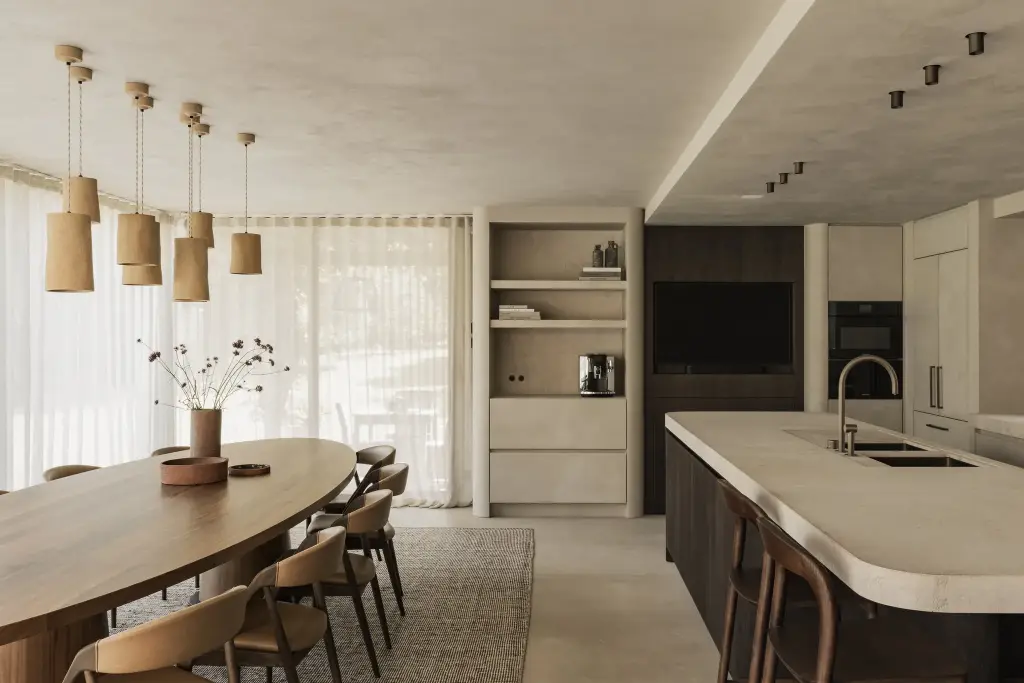 Eetkamer met lange ovale notelaren tafel, hanglampen in aardewerk en keukeneiland met natuurstenen blad, Hoeve in Hansbeke, interieur Laura Calleeuw
