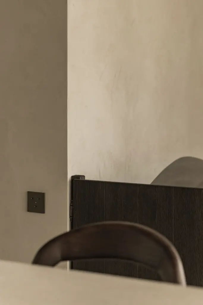 Gepleisterde wand met schakelaar en de rug van een barkruk, Hoeve in Hansbeke, interieur Laura Calleeuw