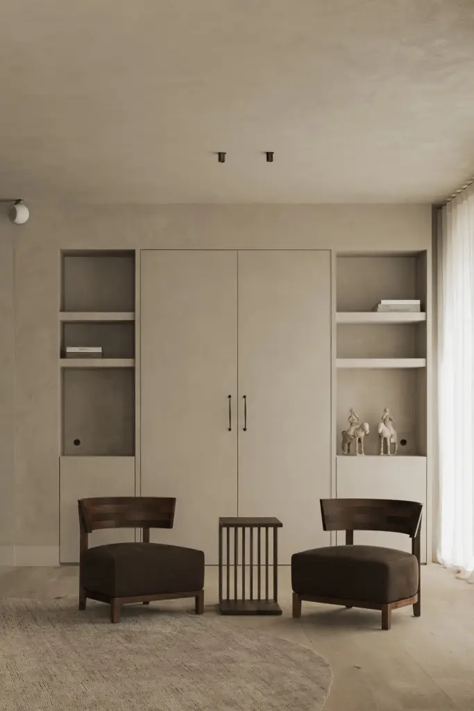 Kastenwand in kalkpleister met verlichte nissen en twee donkere fauteuils met een bijzettafeltje, Hoeve in Hansbeke, interieur Laura Calleeuw