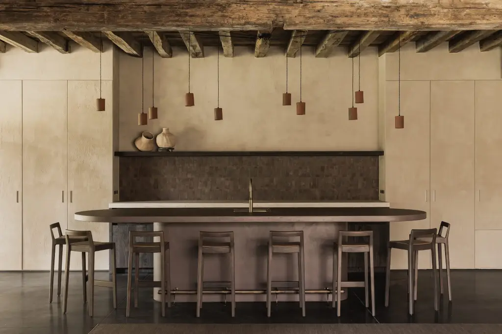Eetbar met ovaal kookeiland, barkrukken, terracotta hanglampen en oude houten balken, Hoeve in Hansbeke, interieur Laura Calleeuw