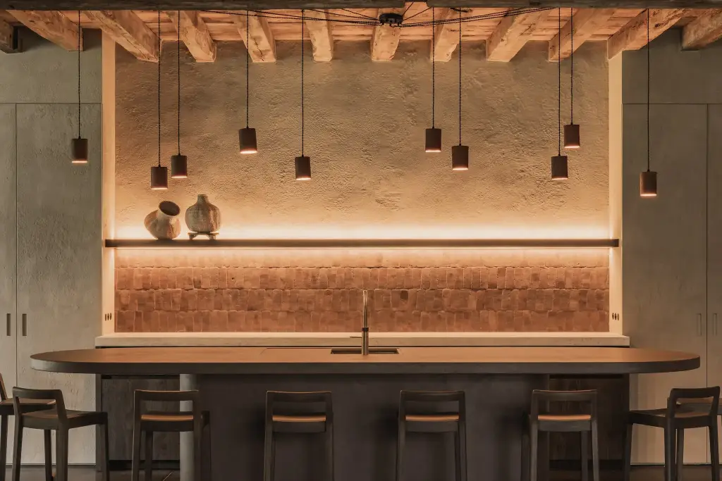 Keukenbar met verlichte terracotta tegelwand, plank met vazen en ovaal kookeiland, Hoeve in Hansbeke, interieur Laura Calleeuw