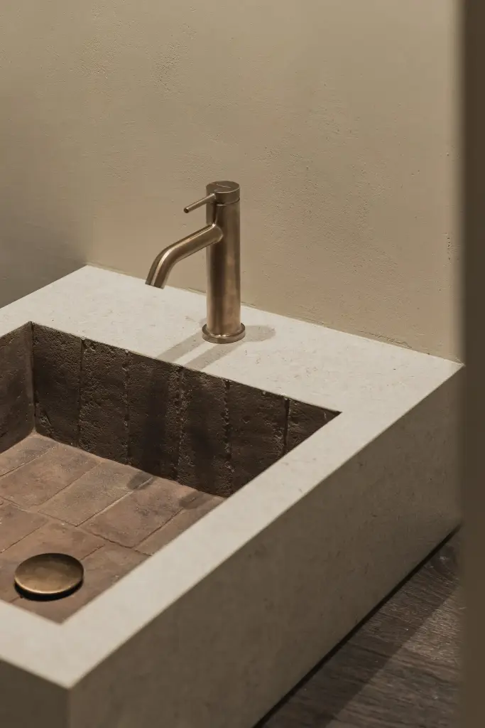 Natuurstenen wastafelzuil met koperen kraan en een spoelbak in terracotta tegels, Hoeve in Hansbeke, interieur Laura Calleeuw
