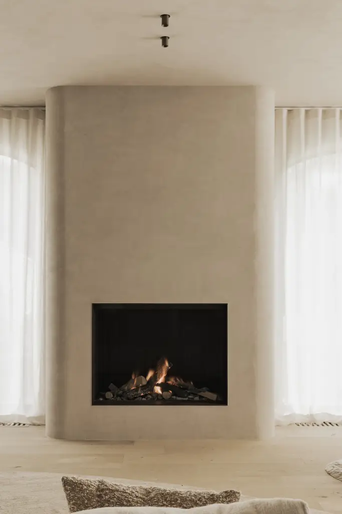 Open haard in een afgerond gepleisterd volume tussen boogvormige vensters met vitrage, Hoeve in Hansbeke, interieur Laura Calleeuw