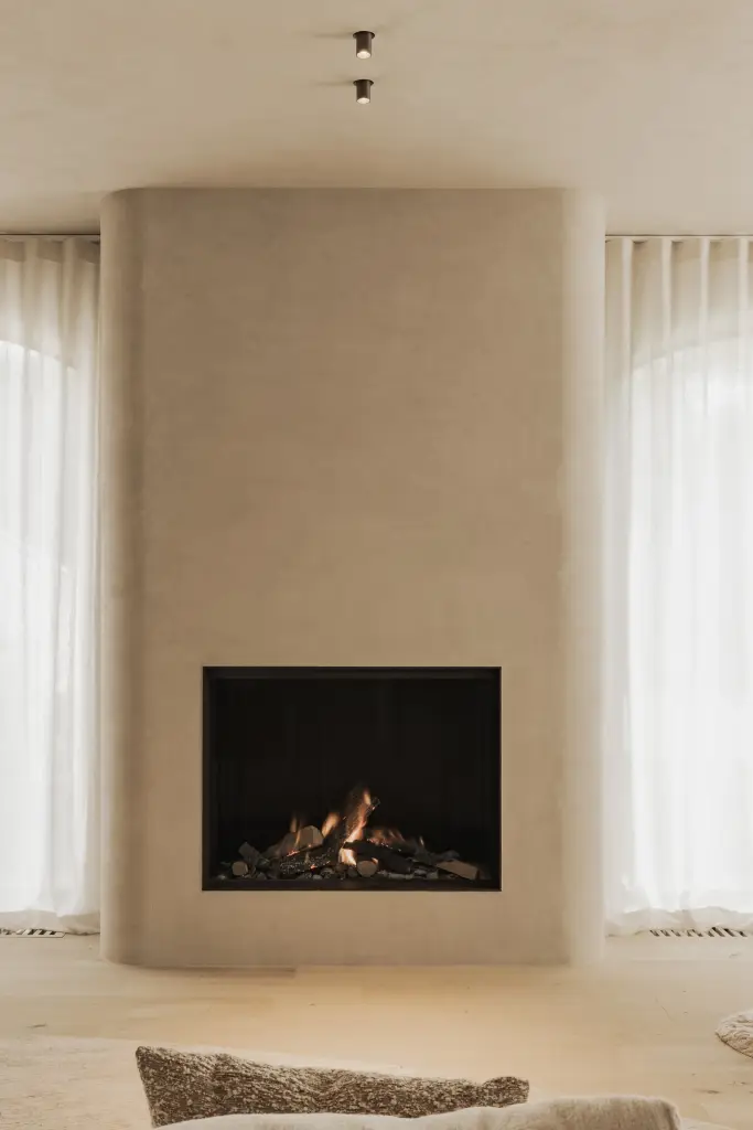 Open haard in een afgerond gepleisterd volume tussen boogvormige vensters met vitrage, Hoeve in Hansbeke, interieur Laura Calleeuw