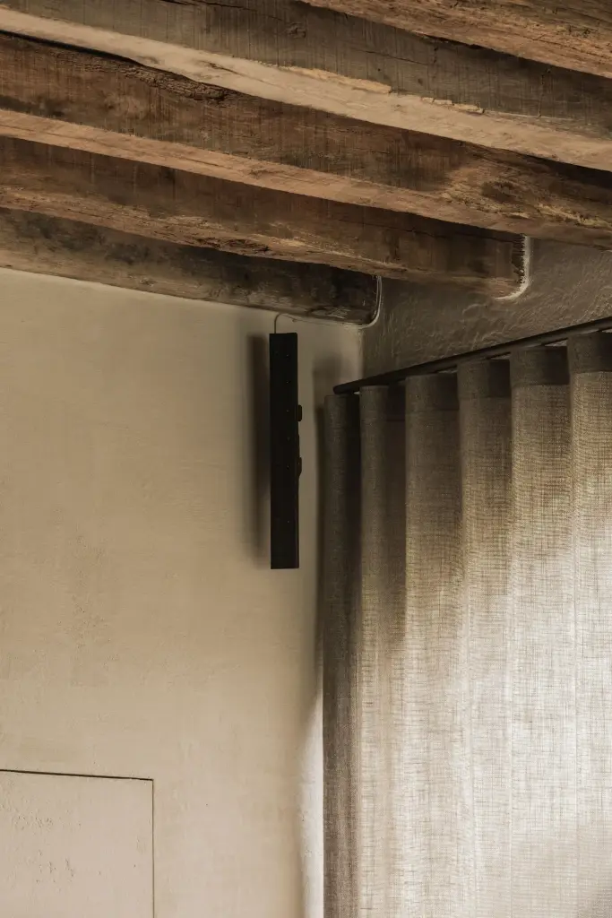 Oude houten balken en een linnen gordijn naast een gepleisterde wand, Hoeve in Hansbeke, interieur Laura Calleeuw
