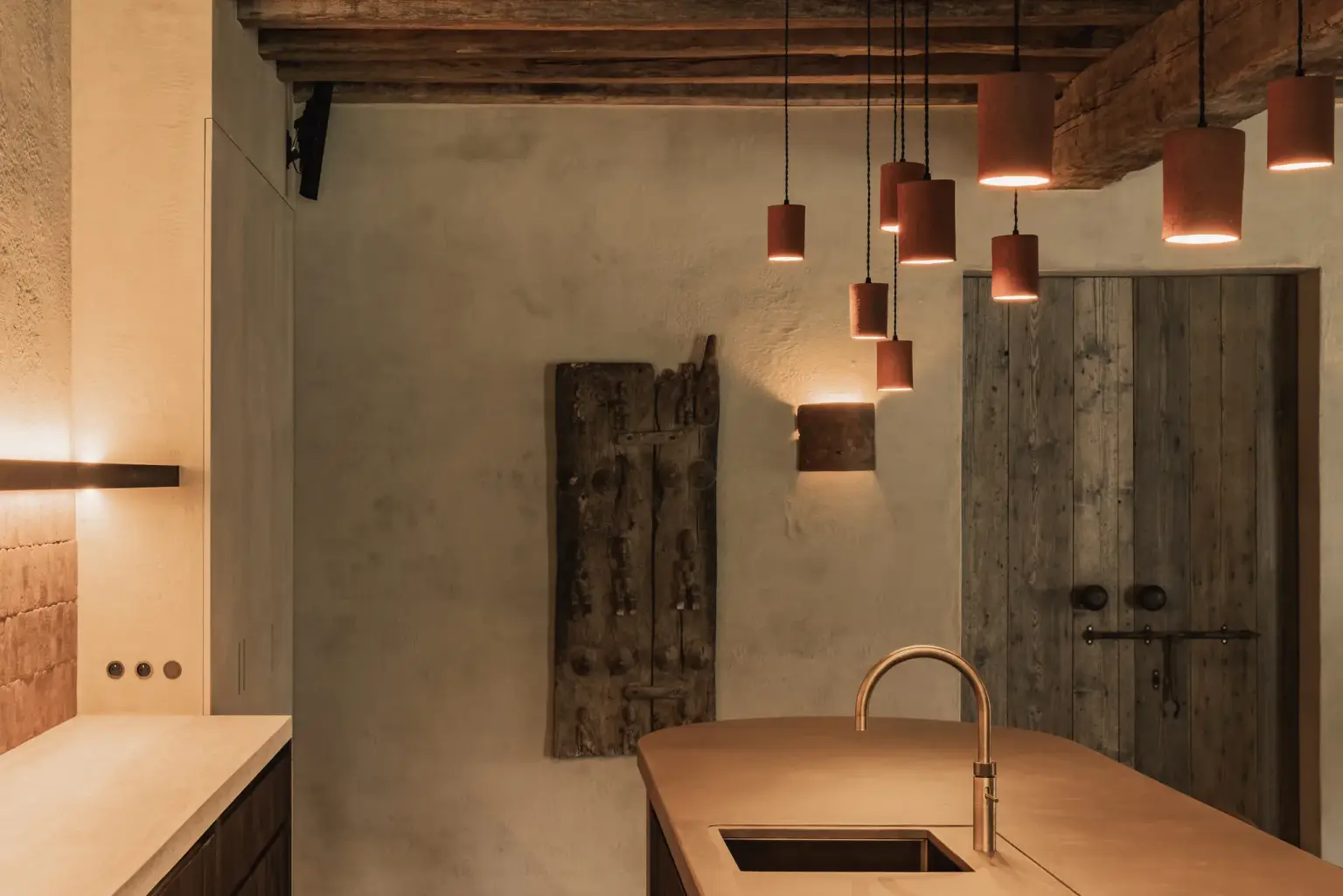 Oude houten deuren naast het keukeneiland met terracotta hanglampen en een messing kraan, Hoeve in Hansbeke, interieur Laura Calleeuw