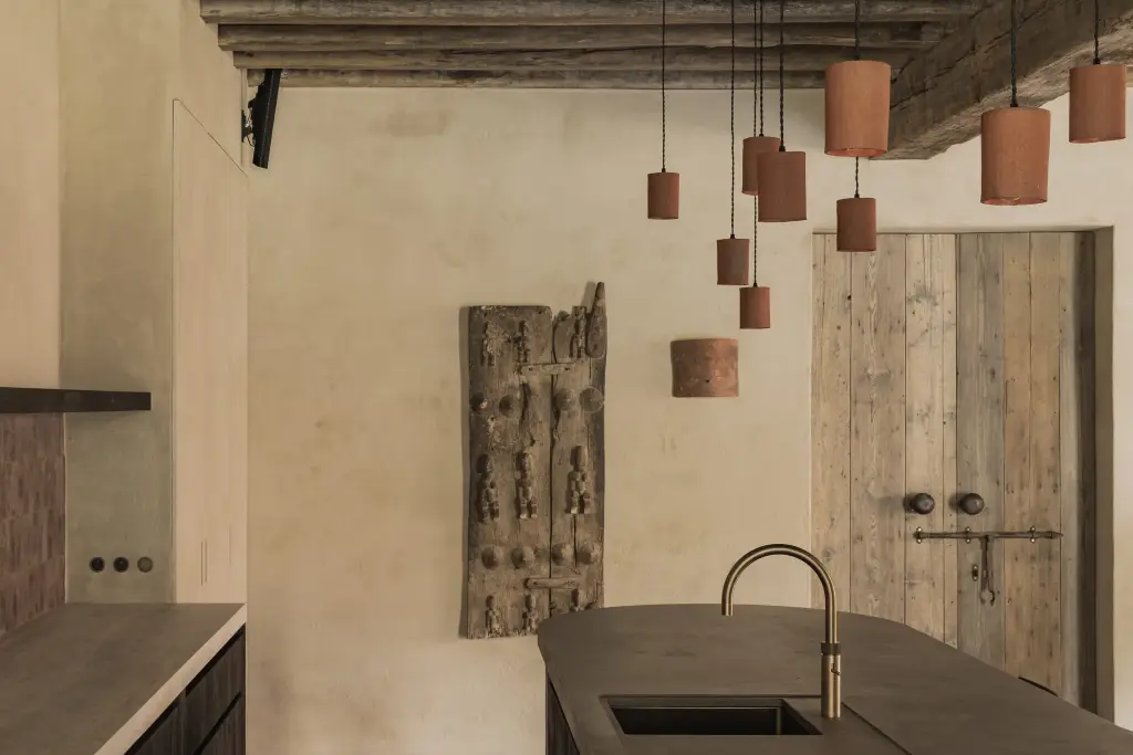 Oude houten deuren naast het keukeneiland met terracotta hanglampen en een messing kraan, Hoeve in Hansbeke, interieur Laura Calleeuw
