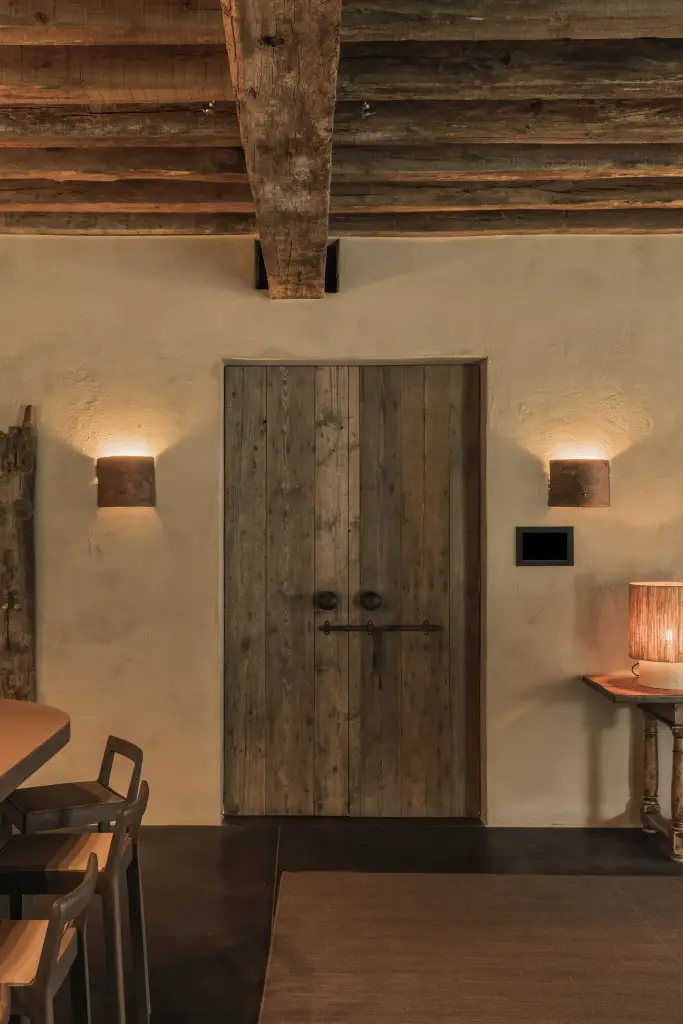 Oude houten dubbele deur met wandlampjes onder zichtbare balken, Hoeve in Hansbeke, interieur Laura Calleeuw