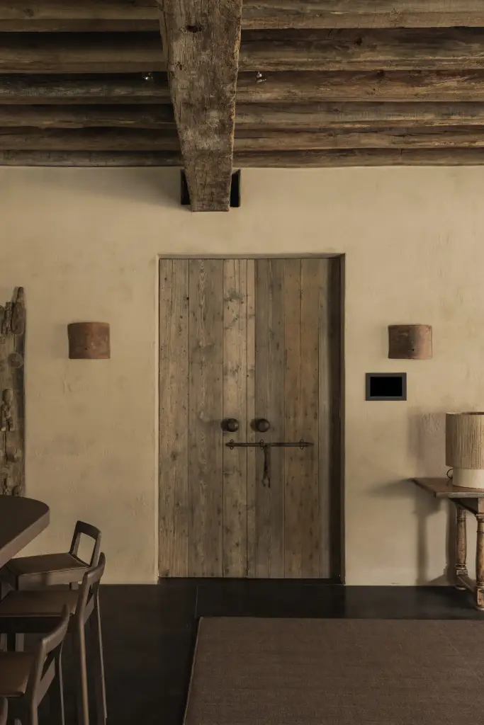 Oude houten dubbele deur met wandlampjes onder zichtbare balken, Hoeve in Hansbeke, interieur Laura Calleeuw