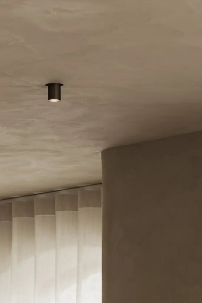 Plafondspot boven een gordijn naast een gepleisterde wand, Hoeve in Hansbeke, interieur Laura Calleeuw