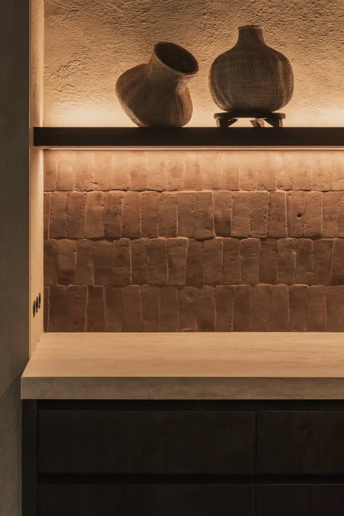 Plank met aarden vazen voor een verlichte terracotta tegelwand, Hoeve in Hansbeke, interieur Laura Calleeuw