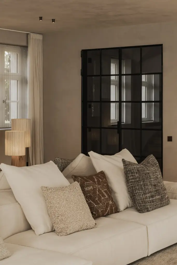 Sofa met kussens in verschillende texturen voor stalen deuren, Hoeve in Hansbeke, interieur Laura Calleeuw