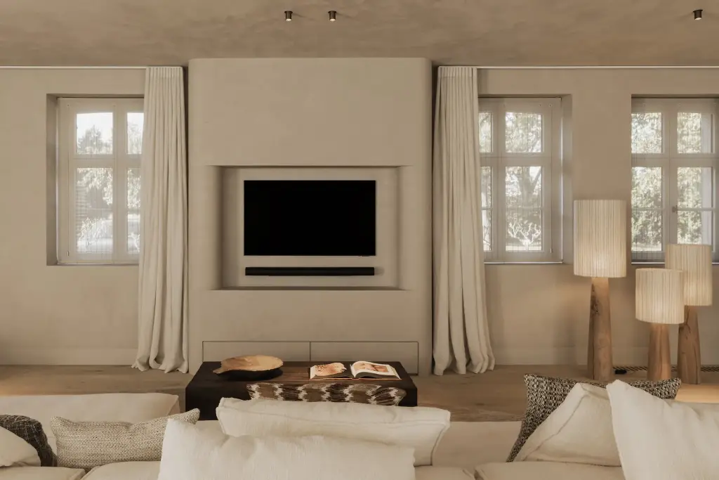 Televisienis in een gepleisterde wand tussen gordijnen, met houten staande lampen en een lage sofa, Hoeve in Hansbeke, interieur Laura Calleeuw