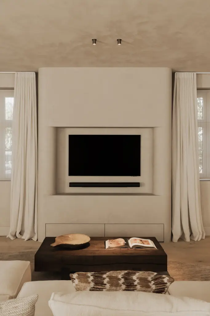 Televisie in een gepleisterde nis boven de donkere salontafel met boek en schaal, Hoeve in Hansbeke, interieur Laura Calleeuw