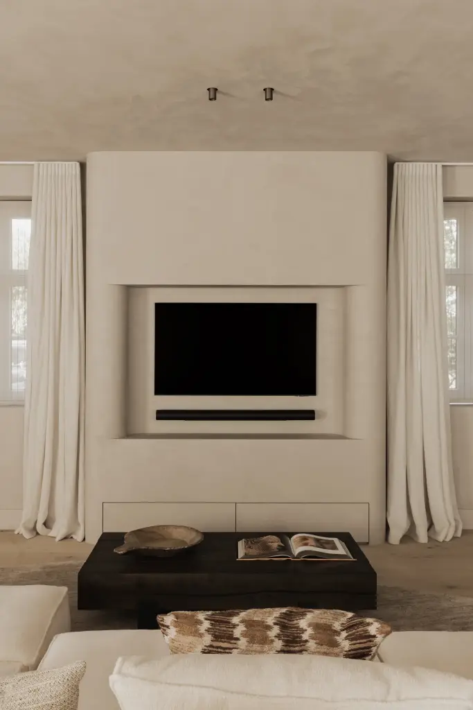 Televisie in een gepleisterde nis boven de donkere salontafel met boek en schaal, Hoeve in Hansbeke, interieur Laura Calleeuw