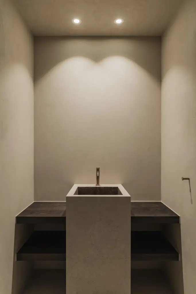 Vrijstaande wastafelzuil in natuursteen onder spots in een gepleisterde nis, Hoeve in Hansbeke, interieur Laura Calleeuw