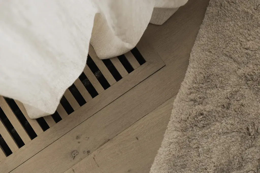 Detail van een ventilatierooster in het eiken parket naast een vachtkleed en linnen beddengoed, Hoeve in Hansbeke, interieur Laura Calleeuw