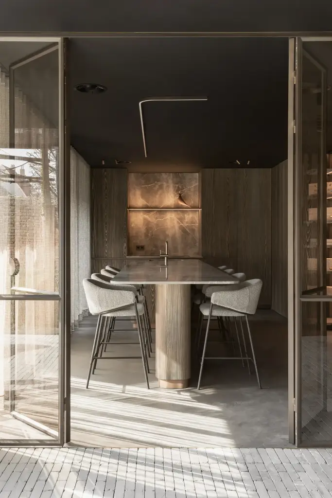 Doorkijk door stalen glasdeuren naar de natuurstenen tafel en het verlichte nisje, a space that changes with the rhythm of the day, interieur Laura Calleeuw