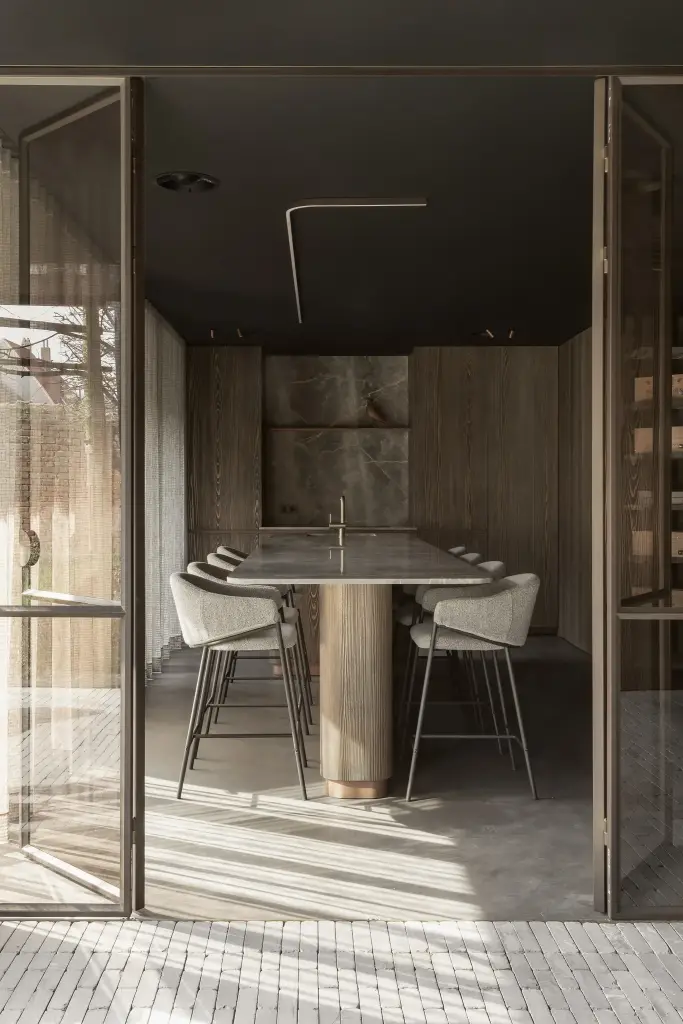 Doorkijk door stalen glasdeuren naar de natuurstenen tafel en het verlichte nisje, a space that changes with the rhythm of the day, interieur Laura Calleeuw