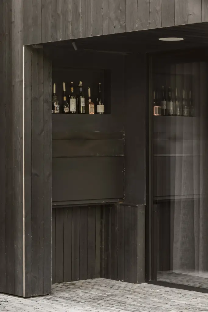 Barnis in donker gebeitst hout met flessen en een glazen deur naast de betonnen tegelvloer, a space that changes with the rhythm of the day, interieur Laura Calleeuw
