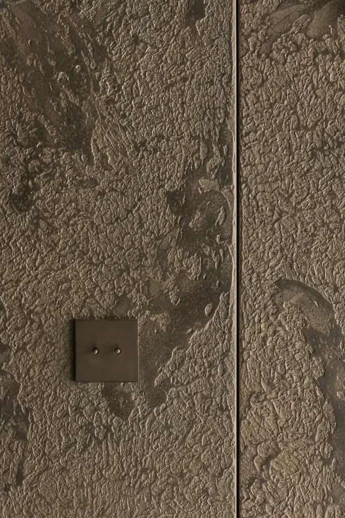 Detail van gestructureerde pleister met een bronzen schakelaar, a space that changes with the rhythm of the day, interieur Laura Calleeuw