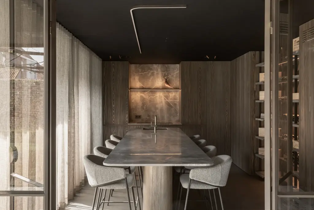 Lange natuurstenen tafel met witte stoelen in een donkere ruimte met stalen glaswanden en wijnrekken, a space that changes with the rhythm of the day, interieur Laura Calleeuw