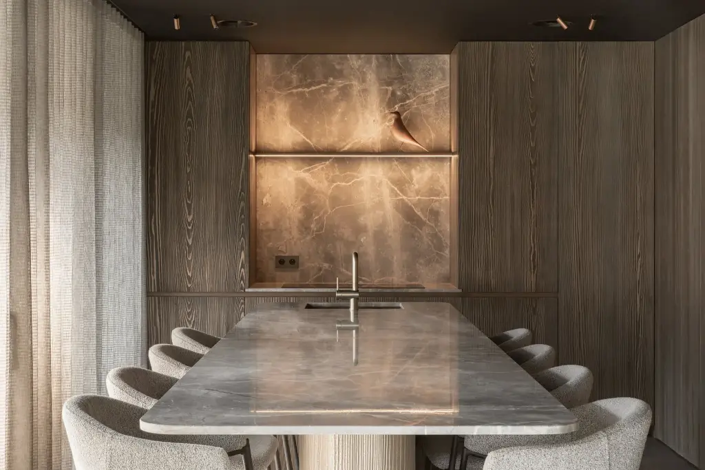 Natuurstenen eettafel met stoelen voor een houten wand met een verlichte natuurstenen nis, a space that changes with the rhythm of the day, interieur Laura Calleeuw