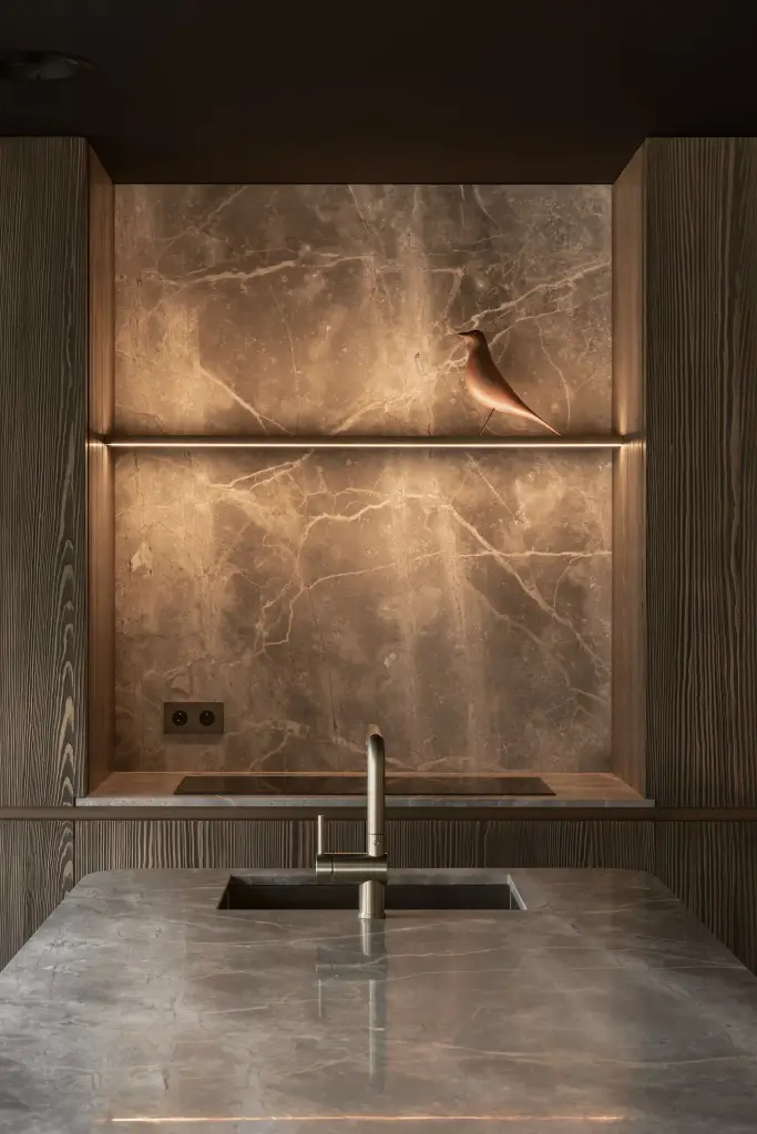 Messing kraan en spoelbak in natuursteen onder de verlichte nis, a space that changes with the rhythm of the day, interieur Laura Calleeuw