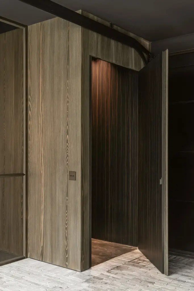 Verborgen deur in de gebeitste houten wand met zicht op een donkere ruimte, a space that changes with the rhythm of the day, interieur Laura Calleeuw