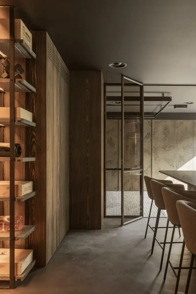 Verlichte houten wijnrekken, stalen glasdeur en barkrukken in de donkere bar, a space that changes with the rhythm of the day, interieur Laura Calleeuw