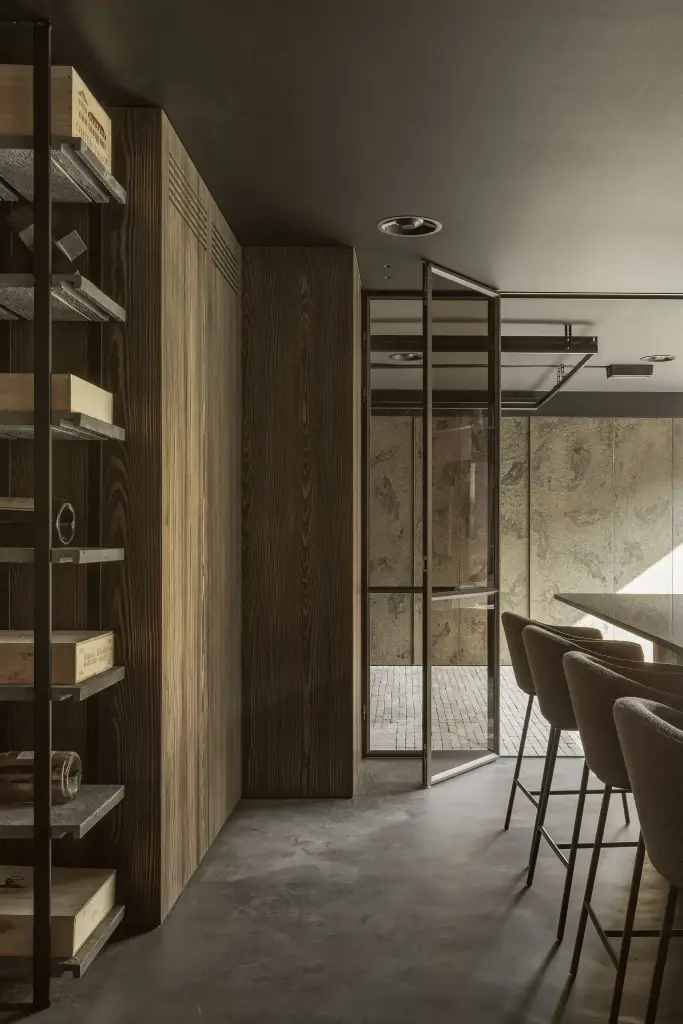 Verlichte houten wijnrekken, stalen glasdeur en barkrukken in de donkere bar, a space that changes with the rhythm of the day, interieur Laura Calleeuw