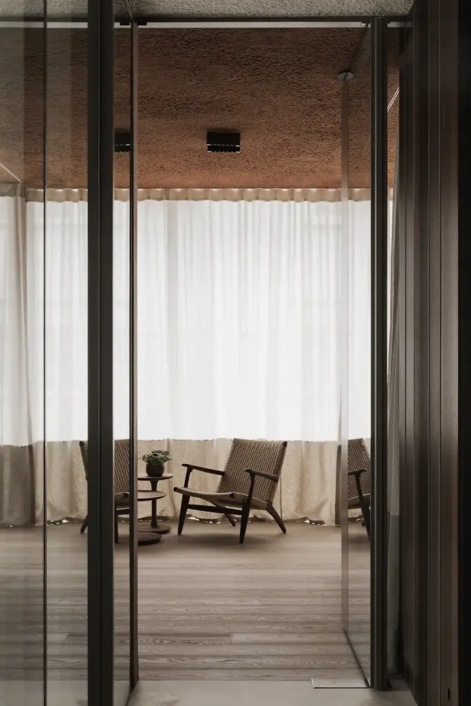 Doorkijk door glazen wanden naar de loungehoek met rieten fauteuil, Kantoor KBC in Ardooie, interieur Laura Calleeuw