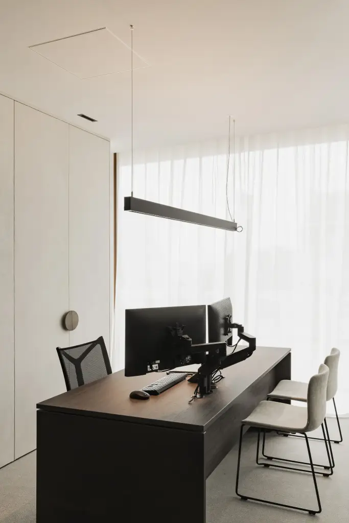 Kantoor met donker houten bureau, schermen op een arm, lange lamp en vitrage, Kantoor KBC in Ardooie, interieur Laura Calleeuw