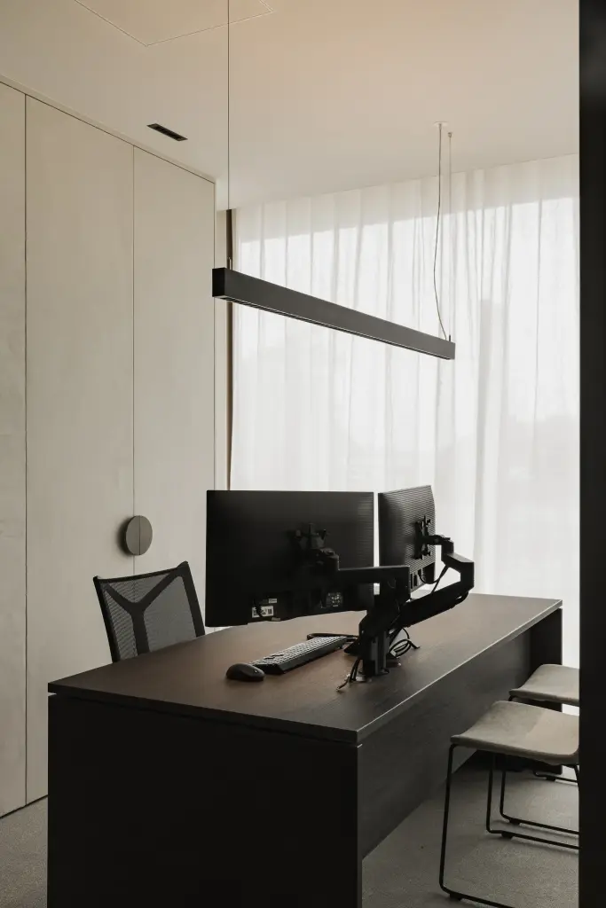 Kantoor met donker houten bureau, schermen op een arm, lange lamp en vitrage, Kantoor KBC in Ardooie, interieur Laura Calleeuw