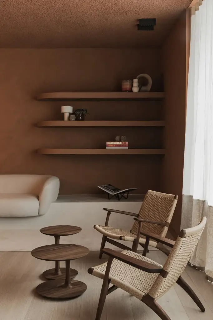 Lounge met rieten fauteuils, houten bijzettafeltjes en planken in een terracotta nis, Kantoor KBC in Ardooie, interieur Laura Calleeuw