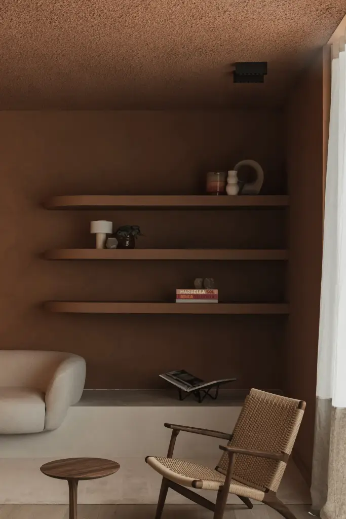 Loungenis met witte sofa, kussen, planken met decoratie en een rieten fauteuil, Kantoor KBC in Ardooie, interieur Laura Calleeuw