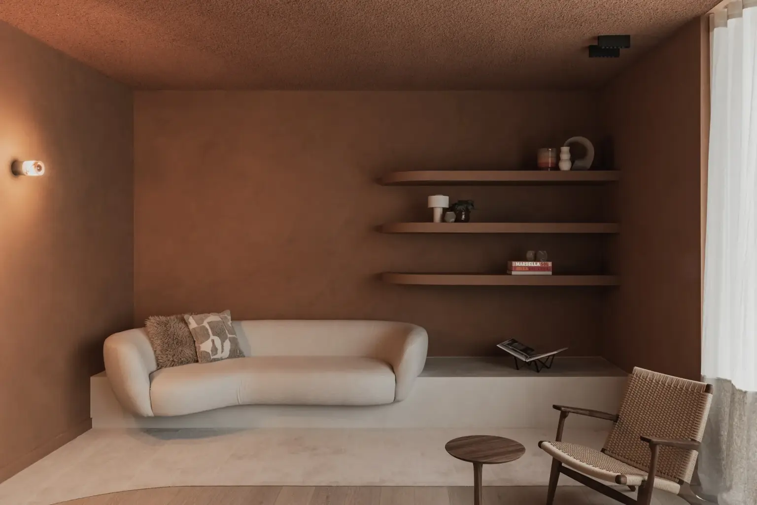 Loungenis met witte sofa, kussen, planken met decoratie en een rieten fauteuil, Kantoor KBC in Ardooie, interieur Laura Calleeuw