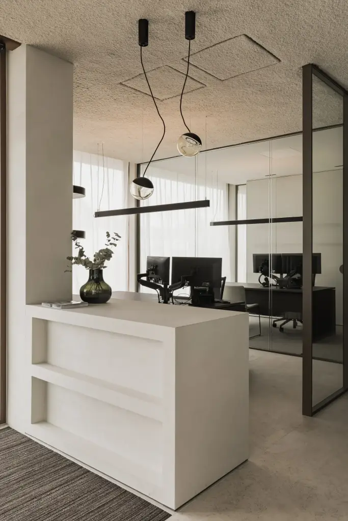 Open kantoor met een witte balie, glazen wanden, hanglampen en werkplekken met schermen, Kantoor KBC in Ardooie, interieur Laura Calleeuw