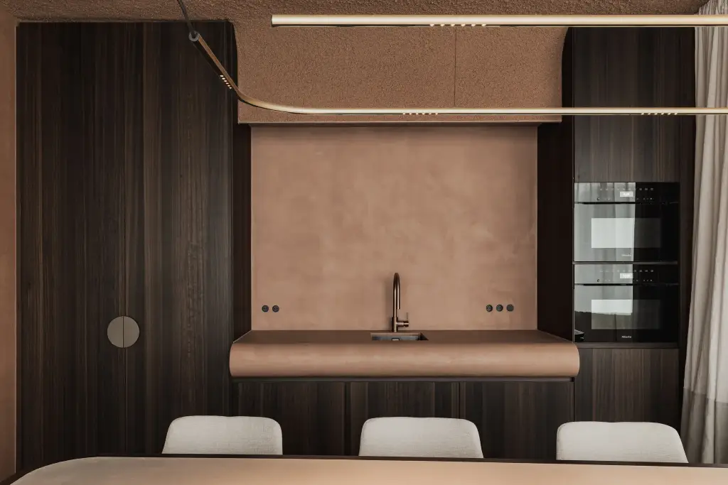 Pantry met terracotta pleisterwand, gebogen blad met spoelbak, inbouwovens en een gouden lichtlijn, Kantoor KBC in Ardooie, interieur Laura Calleeuw