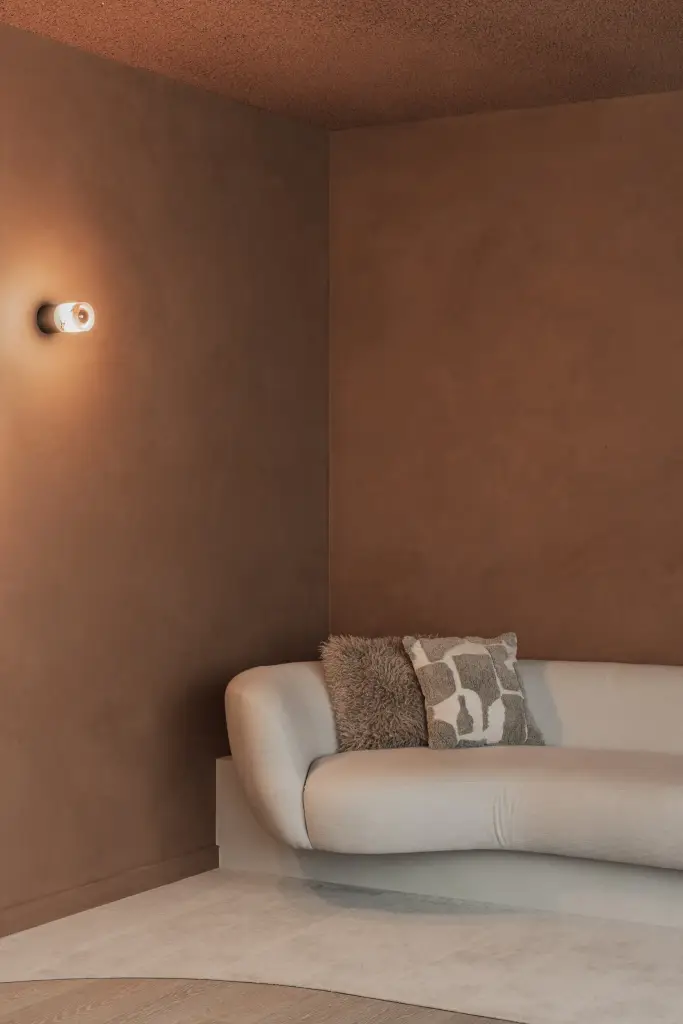 Sofa met kussens en een ronde wandlamp in de terracotta nis, Kantoor KBC in Ardooie, interieur Laura Calleeuw