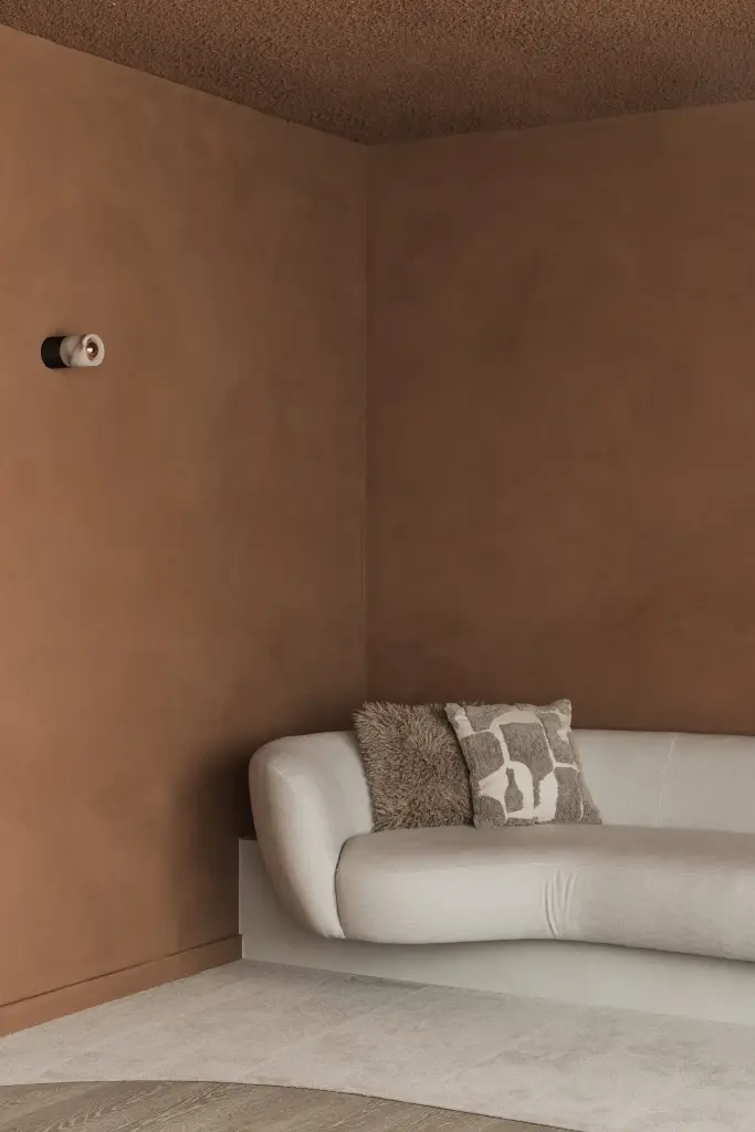 Sofa met kussens en een ronde wandlamp in de terracotta nis, Kantoor KBC in Ardooie, interieur Laura Calleeuw