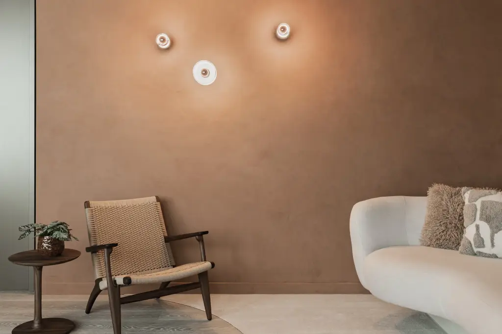 Terracotta pleisterwand met drie ronde wandlampjes, rieten fauteuil en een sofa, Kantoor KBC in Ardooie, interieur Laura Calleeuw