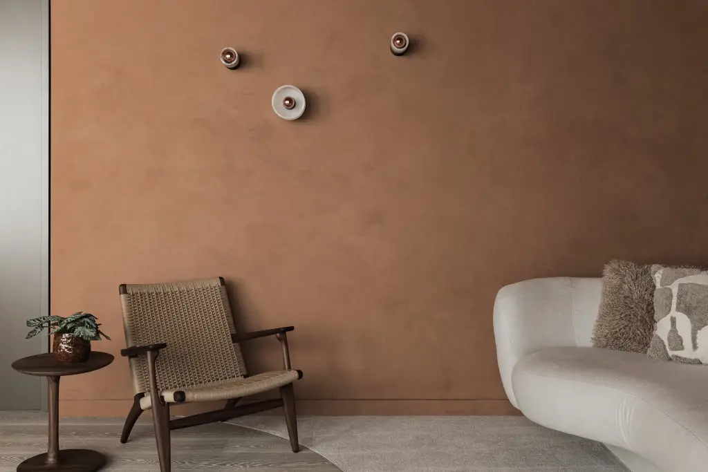 Terracotta pleisterwand met drie ronde wandlampjes, rieten fauteuil en een sofa, Kantoor KBC in Ardooie, interieur Laura Calleeuw