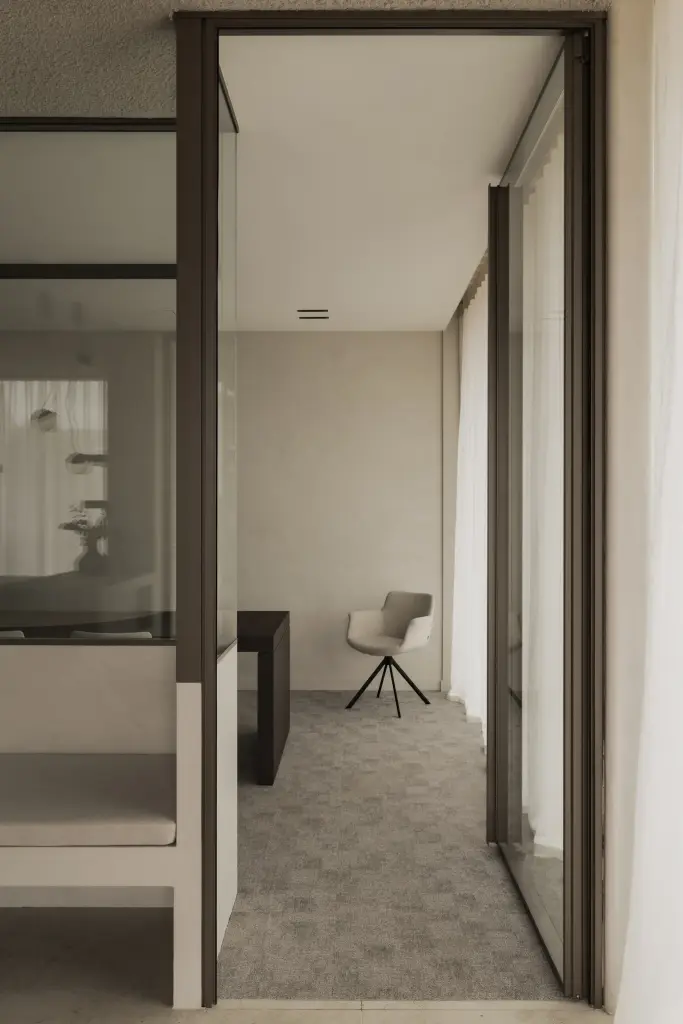 Kleine vergaderkamer met glazen pivotdeur, bank en een stoel, met de deur dicht en open, Kantoor KBC in Ardooie, interieur Laura Calleeuw