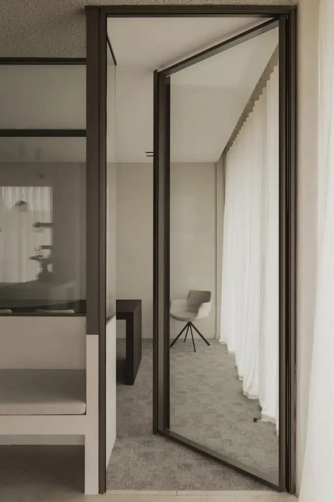 Kleine vergaderkamer met glazen pivotdeur, bank en een stoel, met de deur dicht en open, Kantoor KBC in Ardooie, interieur Laura Calleeuw