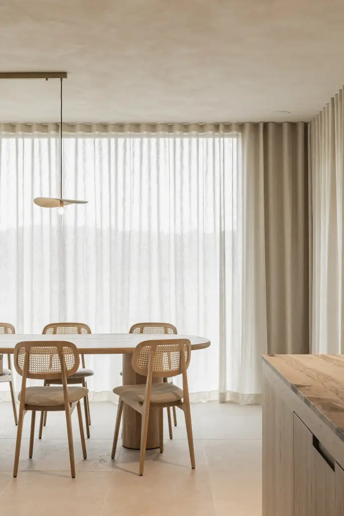 Rotan eetstoelen aan de ovale eiken tafel voor het gordijn, where architecture creates space for experience, interieur Laura Calleeuw